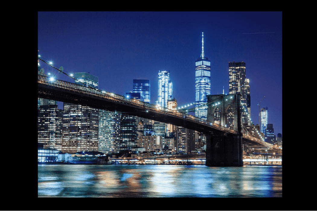 Stunning view of a bridge leading into downtown Manhattan and the financial center, illuminated by the glowing lights of buildings and offices as night falls. The scene evokes excitement and aspirations for a successful and prosperous future.