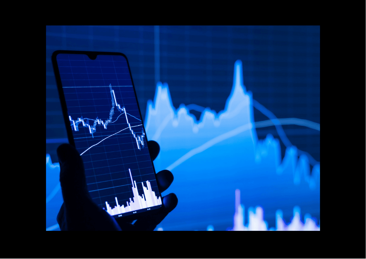 Image in cool blue and cyan tones on a dark background, showing a hand holding a smartphone displaying asset price charts with indicators.