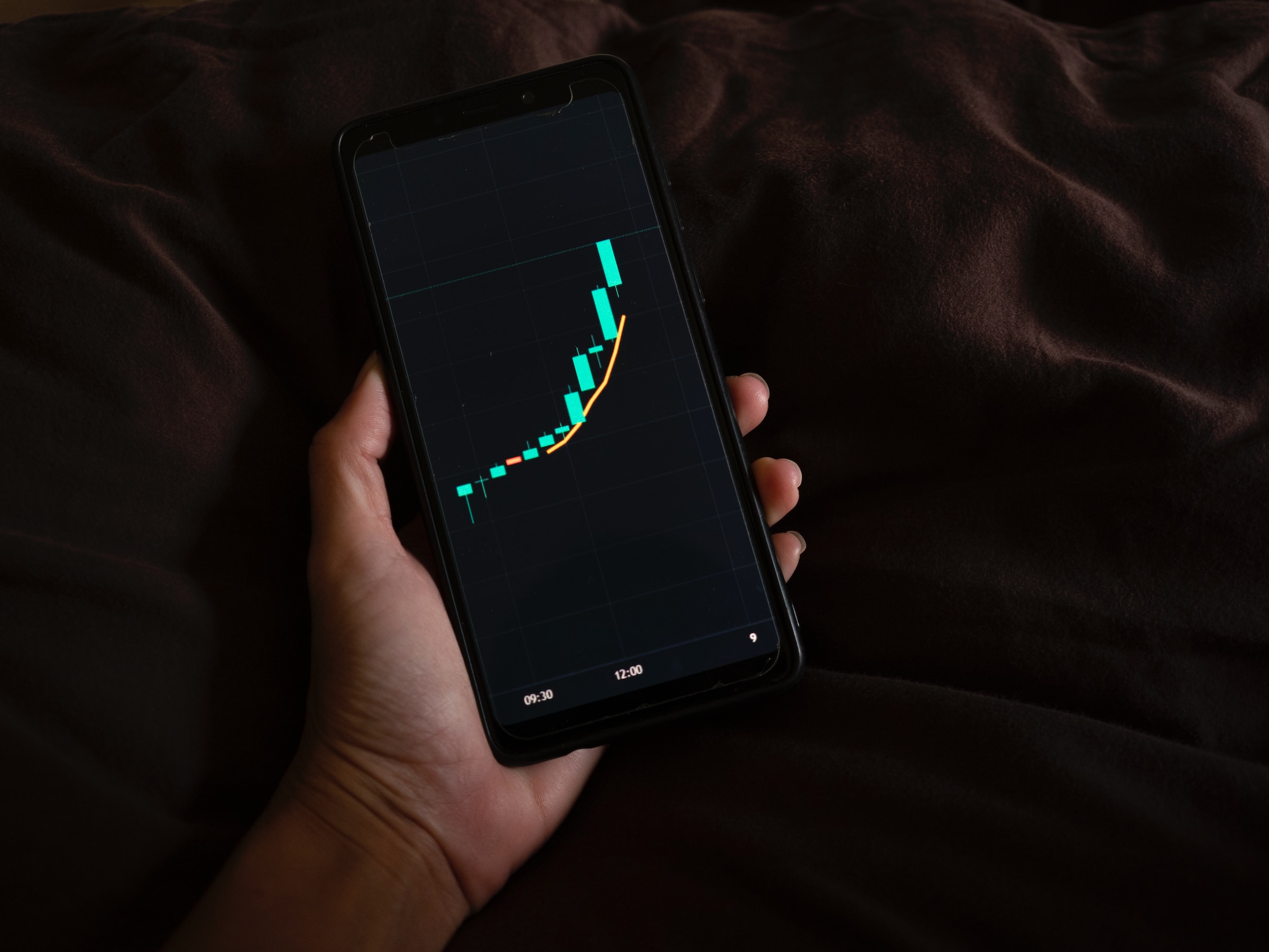 Another image on a dark background, showing a hand holding a smartphone displaying asset price charts with indicators.